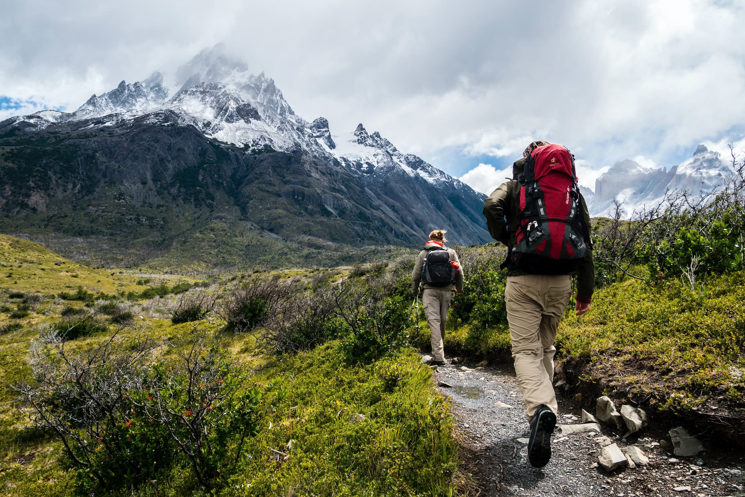 Two hikers walking toward a snow-covered mountain